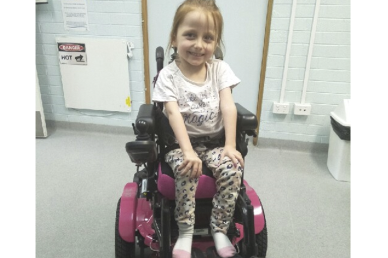 Alexis smiling in her wheelchair in hospital